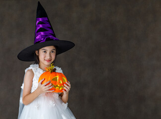 Portrait close up studio shot of Asian cute little girl in witch dress costume with tall hat stand...