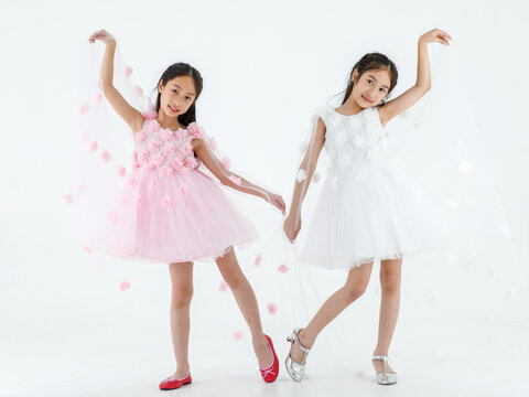 Portrait isolated studio shot of two little Asian ballerina kids in pink and white beautiful roses flowers ballet dress red shoes and high heels smile look at camera pose dance swan gesture together