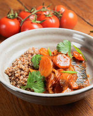 Buckwheat porridge with fish in a ceramic plate over rustic wooden background.