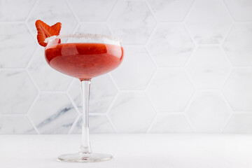 Tropical fresh strawberry juice with pulp in high glass goblet decorated sugar rim, fruit slice in modern white restaurant interior.