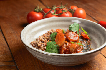 Buckwheat porridge with fish in a ceramic plate over rustic wooden background.
