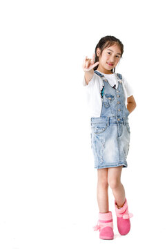 Portrait close up isolated studio shot of young pretty cute girl in jeans denim skirt overalls standing look at camera hold hands up overhead show two fingers peace sign in front of white background