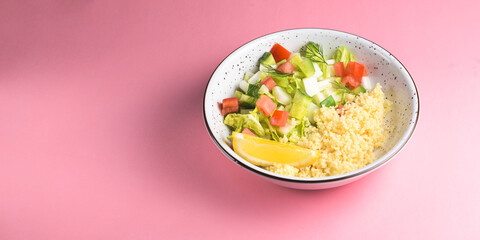Bulgur with vegetables in a plate over pastel pink background. Delicious healthy dish in a bowl