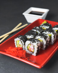Tasty and fresh sushi set served in a red plate with wooden chopsticks. Close-up, selective focus on sushi.