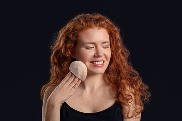 Beautiful young woman with makeup sponge on dark background