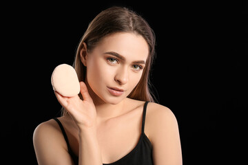 Beautiful young woman with makeup sponge on dark background