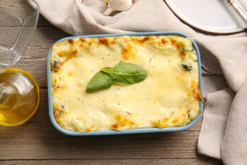 Baking dish with tasty green lasagna on wooden background