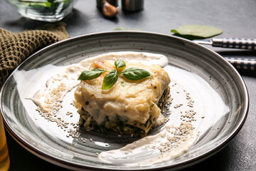 Plate with tasty green lasagna and sauce on dark background, closeup