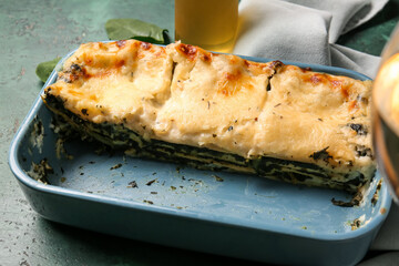 Baking dish with tasty green lasagna on color background