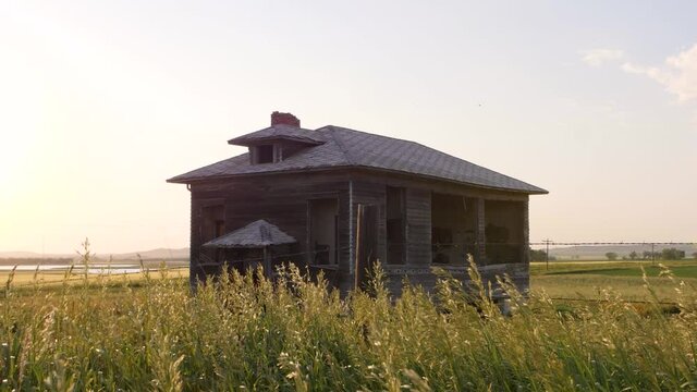 Slow motion shot of old abandoned country schoolhouse with prairie grass blowing in the wind