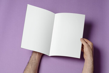 Hands opening A4 catalog on purple background, mock-up series template ready for your design