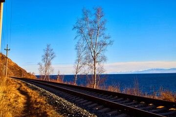 Fototapeta premium Circum Baikal railway running along the shore of Lake Baikal on an autumn sunny day with a yellow landscape around