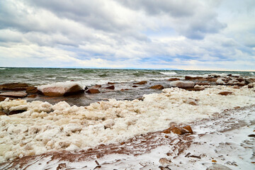 Nature landscape with dramatic sky and clouds, lake with ice, shore with snow and dark trees in...