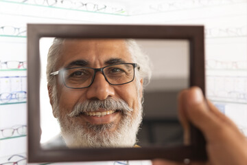 A HAPPY OLD MAN LOOKING AT MIRROR WHILE TRYING ON NEW SPECS