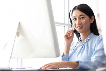 Happy Asian woman operator and team working with headsets and desktop computer at telemarketing customer service. callcenter