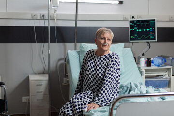 Portrait of sick senior patient getting recovery treatment from intravenous line sitting on...