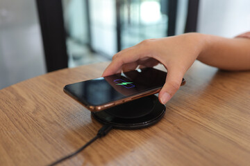 Charging mobile phone battery with wireless device in the table. Smartphone charging on a charging pad. Mobile phone near wireless charger.