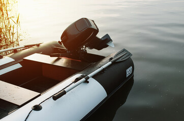 Inflatable motor boat on the water near the shore, outside. Calm water, sunset, selective focus....