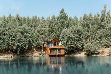 Modern aesthetic wooden house on the lake. Exterior of a country house, cottage on the water near the forest, summer day.