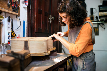 woman luthier making guitars in her musical instrument workshop - obrazy, fototapety, plakaty