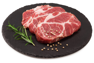raw pork meat with rosemar, tomato and peppercorn on black round stone plate isolated on white background. Clipping path and full depth of field