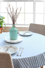 Vase with willow branches on table in dining room