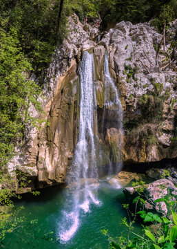 A scenic stream of a waterfall falling among a rocky gorge on the Agur river. Sheer cliffs among lush bushes and trees. Khosta microdistrict, Russia. Travelling, hiking and recreation in mountains.