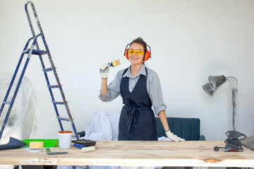Young dark-haired woman in glasses gloves and headphones smiling ready to work in construction workshop