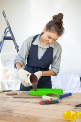 Young dark-haired woman in gloves smiling stirring and pours paint indoors