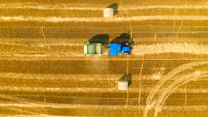 Aerial view of tractor tow trailed bale machine to collect straw from harvested field