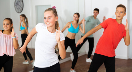 Portrait of cheerful teenage girl practicing dance movements with group of teens in choreography class