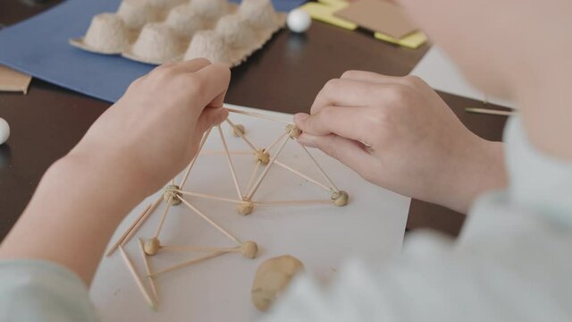 Over-shoulder of unrecognizable person building miniature model using plasticine and wooden toothpicks