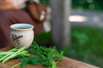 Clay cup on a wooden cutting board with green edible plants. Traditional way of making food