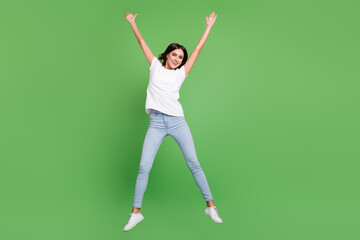 Full length photo of funny brunette young lady jump wear t-shirt jeans isolated on green color background