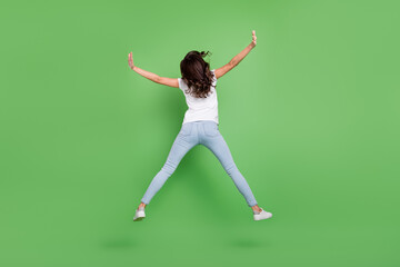 Fototapeta na wymiar Full body back photo of cool brunette young lady jump wear t-shirt jeans isolated on green color background