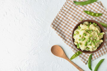 Bowl with mashed potatoes, green peas and spoon on light background