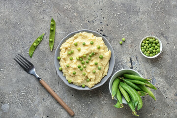Bowl with mashed potatoes, green peas and fork on grunge background