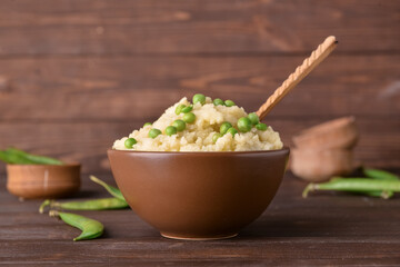 Bowl with mashed potatoes and green peas on wooden background