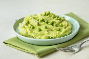 Plate with mashed potatoes, green peas and fork on light background