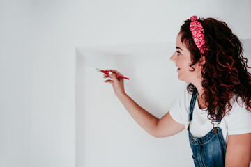 happy caucasian woman painting the room walls with white color. Do it yourself and new home concept