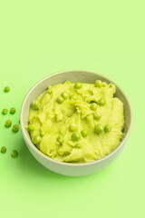 Bowl with mashed potatoes and green peas on color background