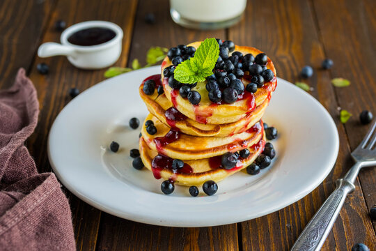 Pancakes with corn flour, blueberries and berry jam on a white plate on a brown wooden background.
