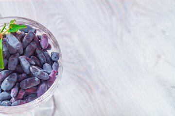 Blue honeysuckle berries in a glass cup on a white wooden table on a sunny day