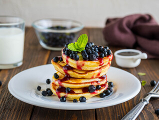 Pancakes with corn flour, blueberries and berry jam on a white plate on a brown wooden background.