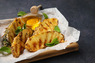 Board with grilled pineapple slices and honey on dark background
