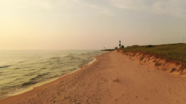 Flying over sand beach on the shore of Lake Michigan at sunset. Ludington State Park, Michigan, United States. Big Sable Point Lighthouse in the background