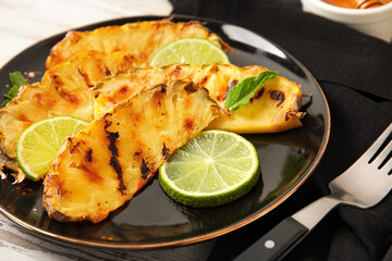 Plate with grilled pineapple slices and lime on light wooden background, closeup
