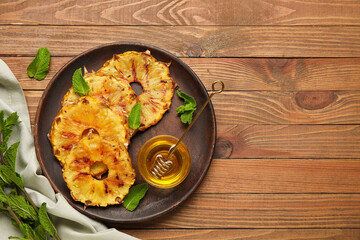 Plate with grilled pineapple slices and honey on wooden background