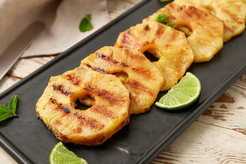 Board with grilled pineapple slices and lime on light wooden background, closeup