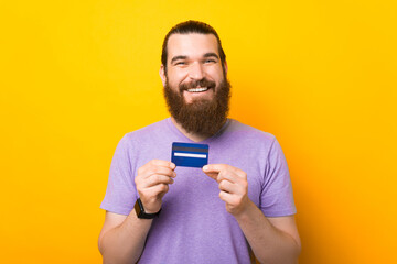Handsome excited young bearded man standing over yellow background, showing credit card